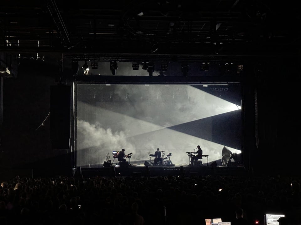 James Blake on the keyboard (far right) together with his drummer (middle) and guitarist performing on stage
