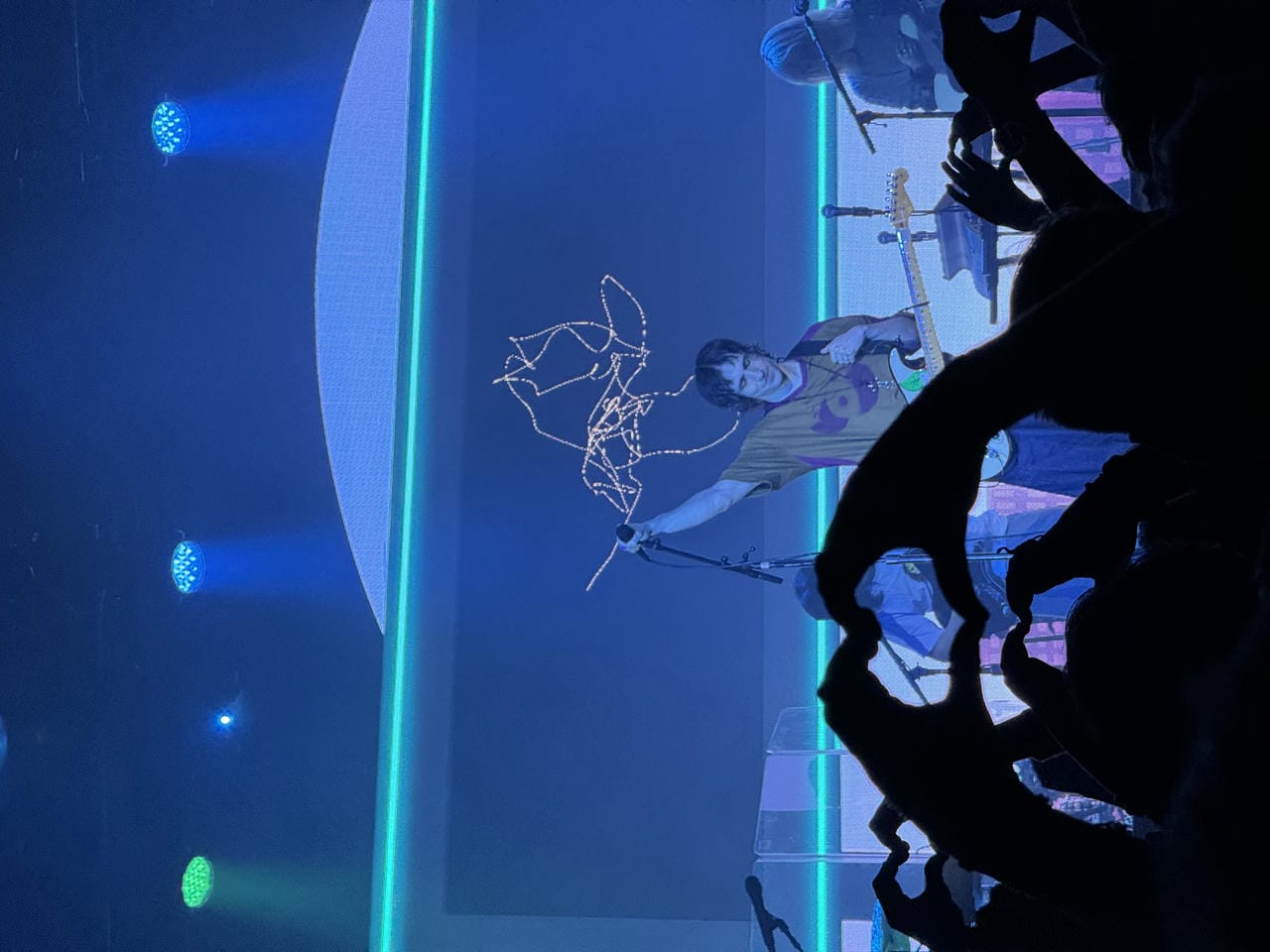 Porter Robinson on stage, with a guitar hanging on his neck. The foreground has multiple people making hearts with their hands